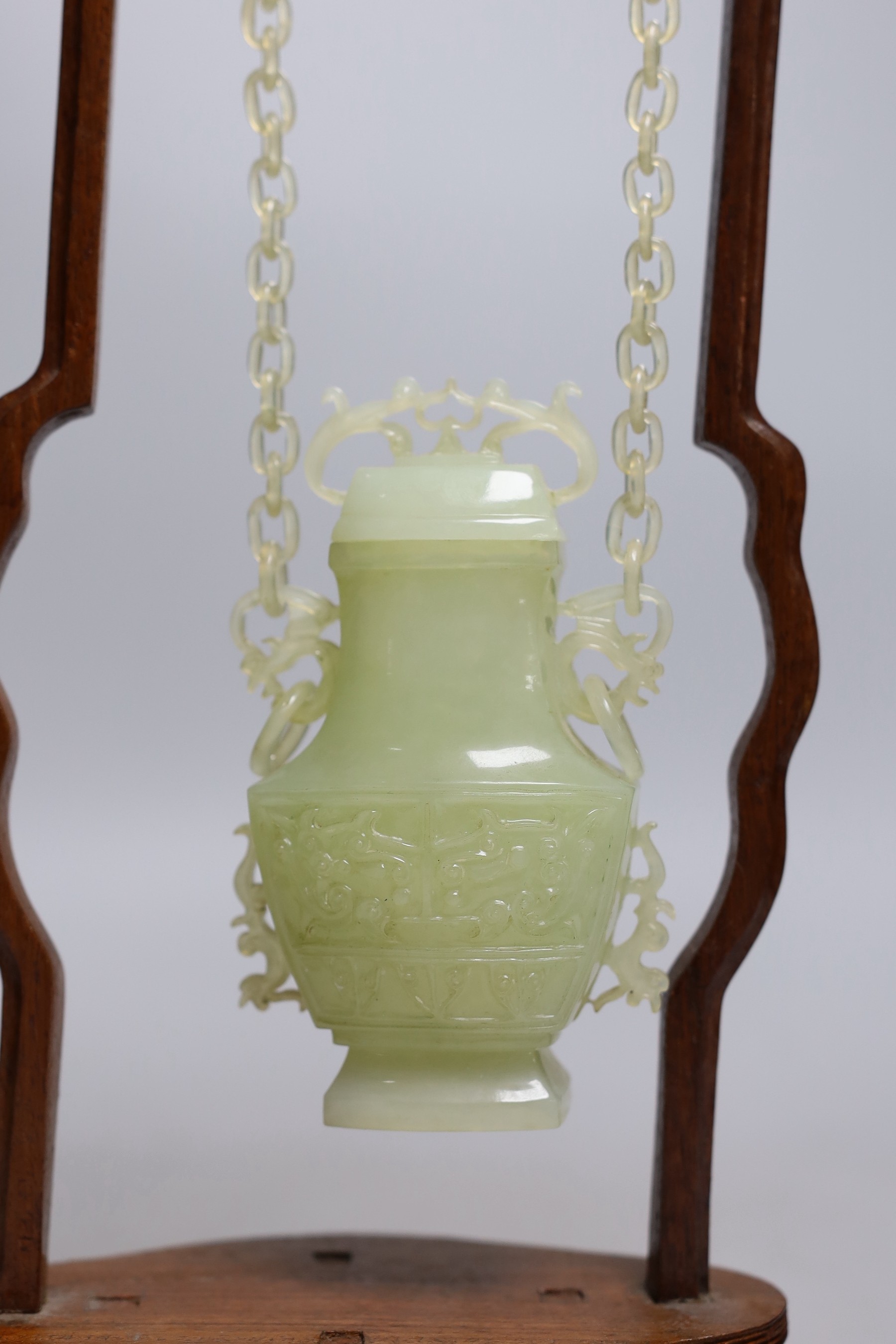 A Chinese bowenite jade hanging vase and cover together with a carved hard wood stand, one foot missing, 42cm tall